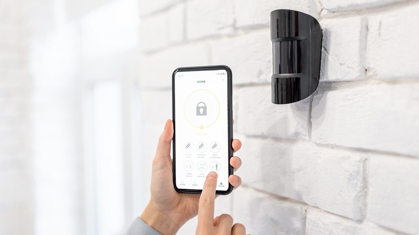 A motion detector on a wall beside a phone showing the alarm app